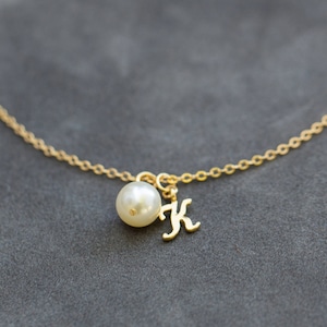 Pu&ograve; includere: Una collana con catena d'oro con una perla e un ciondolo con la lettera K in oro.
