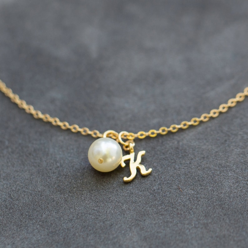 Pu&ograve; includere: Una collana con catena d'oro con una perla e un ciondolo con la lettera K in oro.