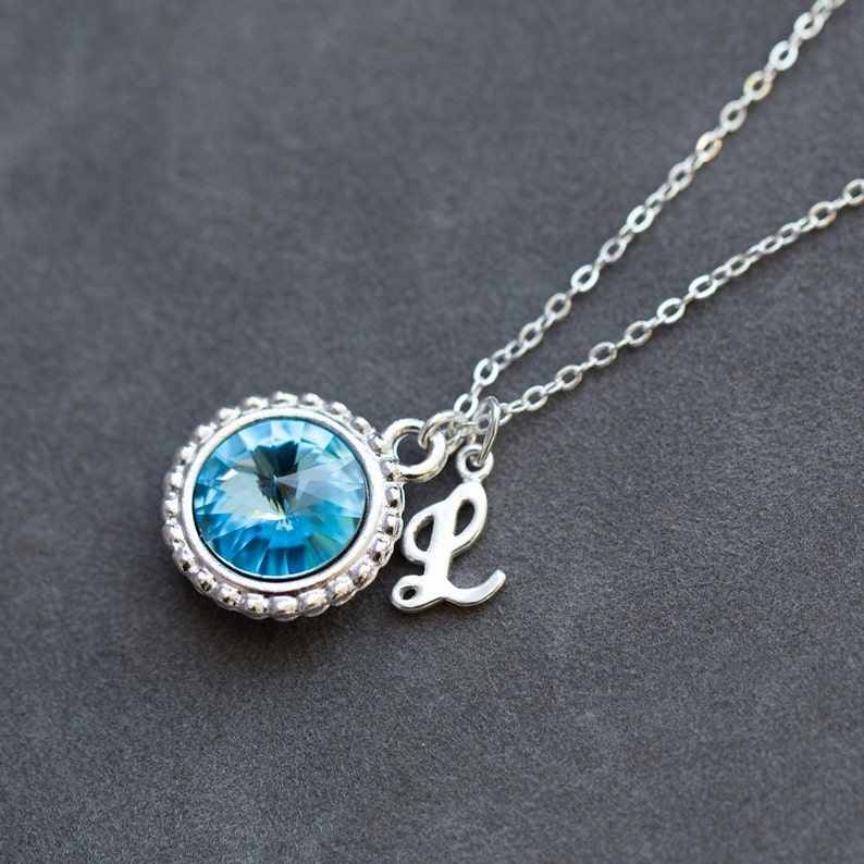 Op de afbeelding: Een zilveren ketting met een blauwe kristallen hanger en een zilveren bedel met de letter L.