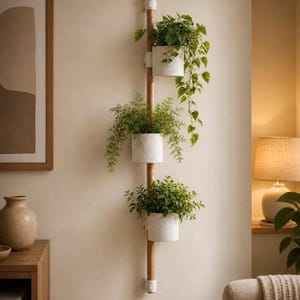 Peut inclure: Un support mural vertical pour plantes composé d'un long poteau en bois avec trois jardinières cylindriques blanches fixées à intervalles. Chaque pot contient une plante verte, celle du haut ayant des tiges retombantes.