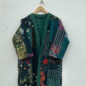 Peut inclure: Longue robe de style kimono en patchwork dans les tons de vert, noir et motifs floraux. La robe est composée de divers morceaux de tissu cousus ensemble, avec une bordure verte unie et une boucle de suspension en haut.
