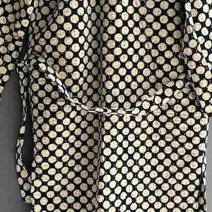 Peut inclure: Une robe noire et cr&egrave;me avec un motif de pois r&eacute;p&eacute;t&eacute;. La robe a une ceinture assortie et est faite d'un tissu doux et matelass&eacute;. Les pois sont de couleur cr&egrave;me et espac&eacute;s uniform&eacute;ment sur le fond noir.