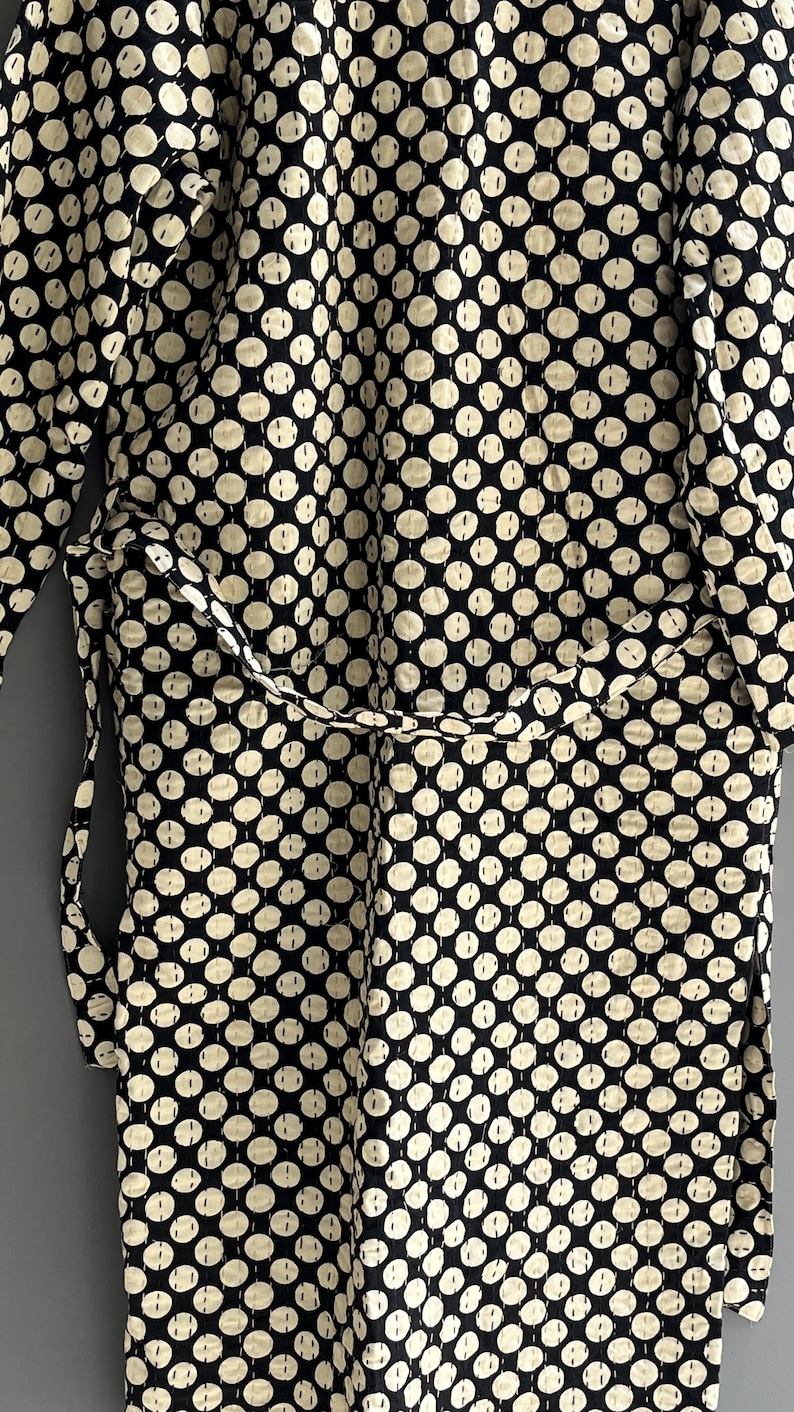 Peut inclure: Une robe noire et cr&egrave;me avec un motif de pois r&eacute;p&eacute;t&eacute;. La robe a une ceinture assortie et est faite d'un tissu doux et matelass&eacute;. Les pois sont de couleur cr&egrave;me et espac&eacute;s uniform&eacute;ment sur le fond noir.