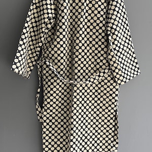 Peut inclure: Robe &agrave; pois noirs et blancs avec une ceinture assortie, suspendue sur un fond gris. La robe a un col et des poignets cr&egrave;me. Les pois sont espac&eacute;s uniform&eacute;ment et couvrent tout le v&ecirc;tement.