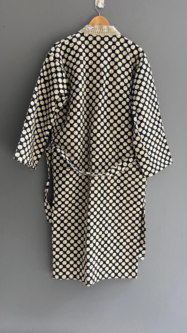 Peut inclure: Robe &agrave; pois noirs et blancs avec une ceinture assortie, suspendue sur un fond gris. La robe a un col et des poignets cr&egrave;me. Les pois sont espac&eacute;s uniform&eacute;ment et couvrent tout le v&ecirc;tement.