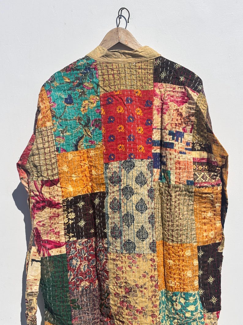 May include: A patchwork jacket with a variety of colorful fabric squares. The jacket features a mix of floral and geometric patterns in shades of teal, red, gold, and brown. The jacket is hanging on a wooden hanger.