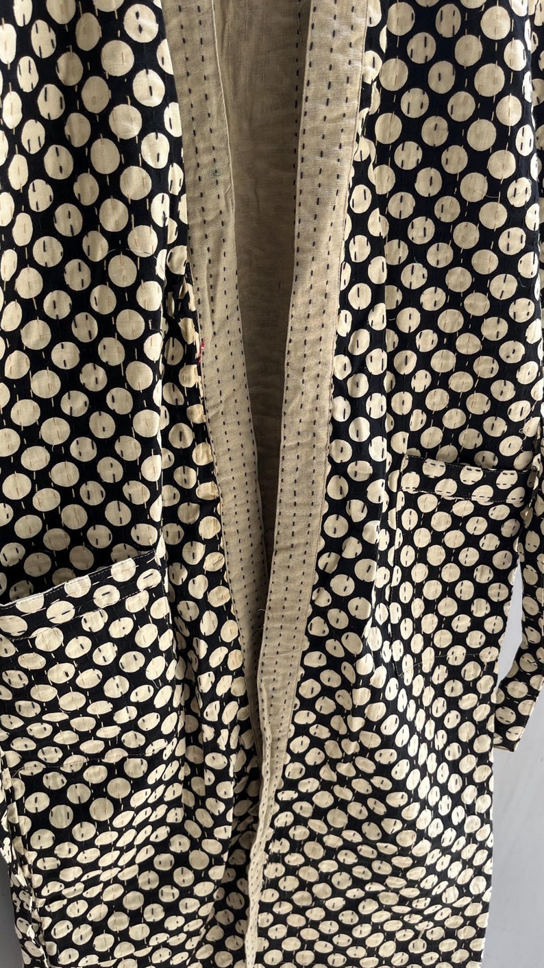 Peut inclure: Longue veste ouverte &agrave; l'avant, orn&eacute;e de pois noirs et blancs. La veste comporte deux poches avant et une doublure cr&egrave;me. Le tissu semble &ecirc;tre matelass&eacute; avec des coutures visibles.