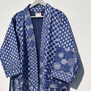 May include: A blue and white patterned kimono-style robe with a variety of geometric designs, including polka dots and circles. The robe is hanging on a wooden hanger against a white background.