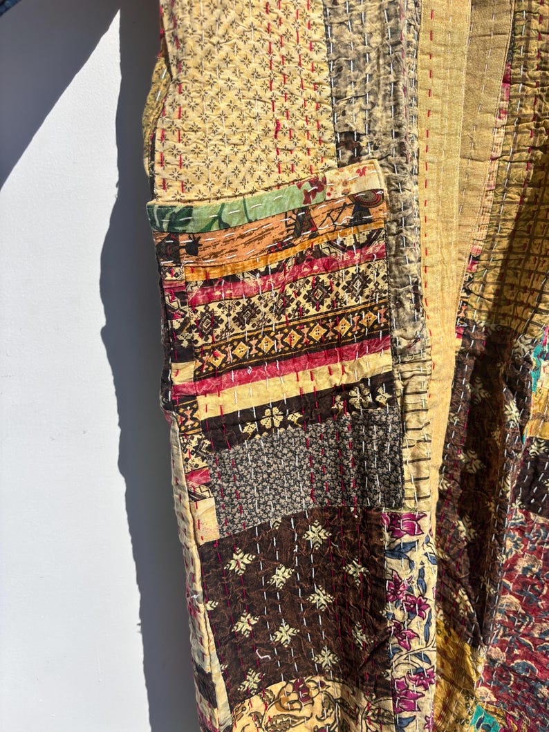 May include: A patchwork jacket in shades of tan, brown, and burgundy. The jacket features a variety of patterned fabrics, including floral and geometric designs, stitched together with visible thread. The jacket has a pocket on the front.