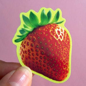 May include: A die-cut sticker featuring a strawberry with a vibrant red body and green leaves. The design utilizes a distinct halftone dot pattern throughout, with a bright yellow outline surrounding the entire fruit shape against a solid background.