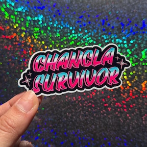 May include: A die-cut sticker featuring the text CHANCLA SURVIVOR in a bold, stylized font. The letters transition from a bright pink at the top to a light blue at the bottom, outlined in black and white, with small four-pointed star accents.