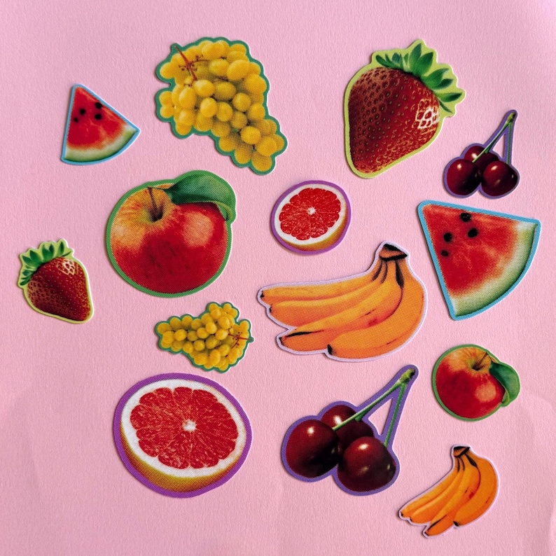 May include: A collection of fruit stickers featuring a red apple, yellow bananas, green grapes, red strawberries, cherries, watermelon slices, and grapefruit halves. Each sticker has a distinct outline, showcasing vibrant colors and realistic fruit textures.