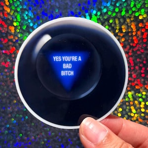 May include: A circular sticker featuring a black sphere design with a white border. In the center, a blue triangle contains the white text 'YES YOU'RE A BAD BITCH', mimicking the appearance of a classic fortune-telling toy with a glossy finish.