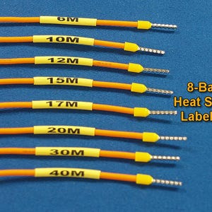 Puede incluir: Un juego de etiquetas termorretráctiles de 8 bandas. El juego incluye cables naranjas con etiquetas amarillas marcadas 6M, 10M, 12M, 15M, 17M, 20M, 30M y 40M. Cada cable tiene un extremo plateado. El fondo es azul liso.