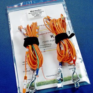 May include: Two coils of orange wire secured with black hook-and-loop straps, featuring metal alligator clips and clear plastic connectors. The components are packaged in a clear plastic bag over an instruction sheet labeled Marauder Band Lined Crosswires.