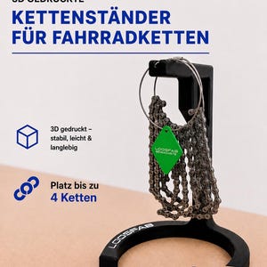 Könnte beinhalten: Ein schwarzer 3D-gedruckter Fahrradkettenständer mit gebogener Basis und vertikalem Arm. Der Ständer trägt den Schriftzug LoosFab auf der Basis und hält eine Fahrradkette, die durch ein grünes rautenförmiges Schild mit der Aufschrift LoosFab Gewachste geführt ist.