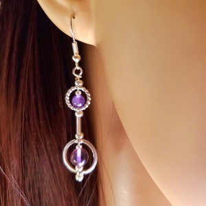 May include: Silver dangle earrings with two purple amethyst stones set in silver circles.