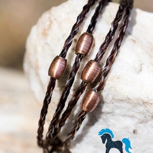 May include: A triple strand bracelet made of brown horsehair with copper beads. The bracelet is on a white rock surface. The text "THE SUGAR LADY HORSE HAIR & LEATHER www.thesugarladystudio.com" is at the bottom of the image.