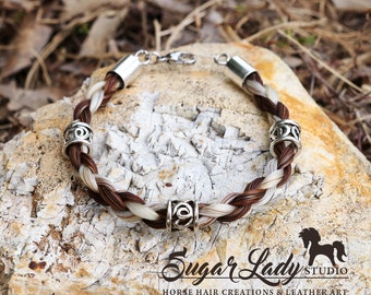 May include: A braided horsehair bracelet with silver beads and a silver clasp. The bracelet is brown, white, and black.