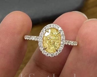 May include: A diamond ring featuring a large, oval-cut yellow diamond center stone surrounded by a halo of smaller, clear diamonds. The band is also set with small diamonds. The ring is held between fingers, with the text "KSentJewel" visible.