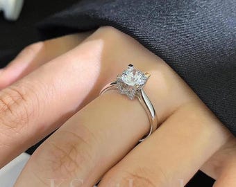 May include: A silver ring with a large, clear, round-cut gemstone as the centerpiece. The ring has a delicate band and is set with smaller accent stones around the main stone. The ring is on a finger.