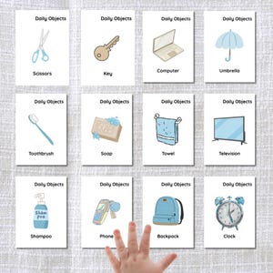 May include: Illustrated flashcards labelled "Daily Objects" showing everyday items. The cards feature images of scissors, a key, a computer, an umbrella, a toothbrush, soap, a towel, a television, shampoo, a phone, a backpack, and a clock.
