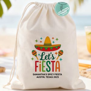 May include: Off-white drawstring bag with a colorful "Let's Fiesta" design. The design includes a sombrero, maracas, and text that reads "Samantha's Spicy Fiesta Austin, Texas 2025". A small, round sticker with text is attached to the bag.