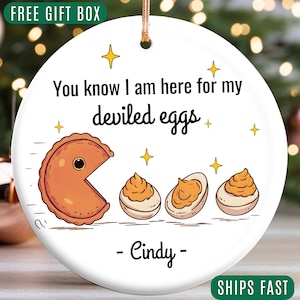 May include: A white ceramic ornament with a Pac-Man-like deviled egg design and the text "You know I am here for my deviled eggs." The ornament includes the name "Cindy" and the words "FREE GIFT BOX" and "SHIPS FAST".