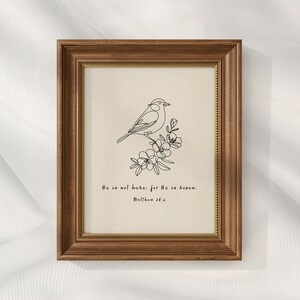 May include: A framed print featuring a line drawing of a bird perched on a flowering branch. The artwork is in black against a cream background, with the text "He is not here: for He is risen. Matthew 28:6."
