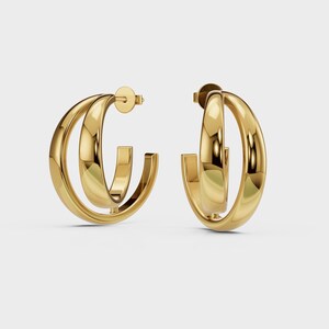 May include: A pair of gold-colored hoop earrings. Each earring features a double-hoop design with a post backing. The earrings have a polished, reflective surface, and are set against a plain white background.