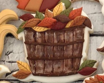 Può includere: Un secchio di legno marrone pieno di foglie autunnali colorate. Il secchio è decorato con un motivo a venature del legno. Le foglie sono in tonalità di rosso, arancione, giallo e marrone.