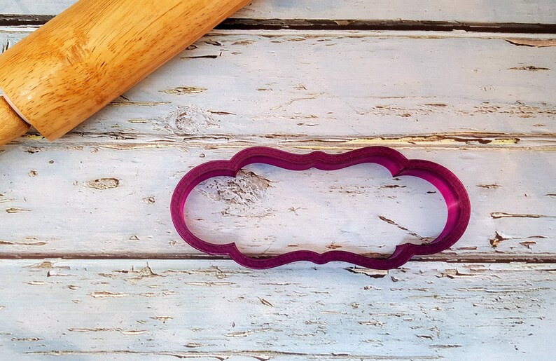 May include: A purple plastic cookie cutter shaped like a banner with a scalloped edge.