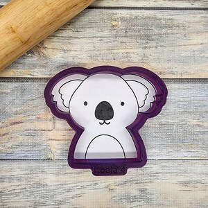 May include: Purple plastic cookie cutter shaped like a koala bear with black eyes and a nose. The cutter has the text "Koala 4" on the bottom.