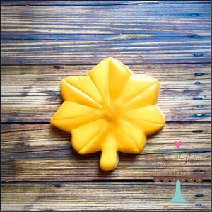 May include: A yellow sugar cookie shaped like a military rank insignia, a star with five points, on a wood background. The cookie is decorated with a yellow icing.
