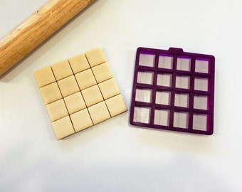 May include: A close-up of a rolling pin and a purple plastic mold with 16 square sections. A sheet of dough is cut into 16 squares.