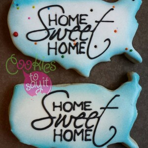 May include: Two blue and white sugar cookies decorated with a white background and black icing. The cookies are shaped like the United States of America and have the words "Home Sweet Home" written on them.