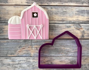 May include: A pink and white barn cookie cutter with a silo on the side. The cutter is made of purple plastic and is shown next to a decorated cookie.