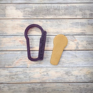 May include: Purple plastic cookie cutter shaped like a microphone with the text "Microphone 3.5" on the side. Next to the cutter is a light brown cookie in the shape of a microphone.