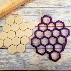 May include: A purple plastic honeycomb cookie cutter and a sheet of dough cut into hexagonal shapes.