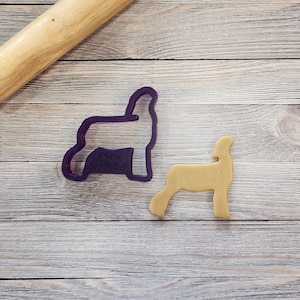May include: Purple plastic cookie cutter shaped like a show lamb. A tan cookie is cut out using the cookie cutter.