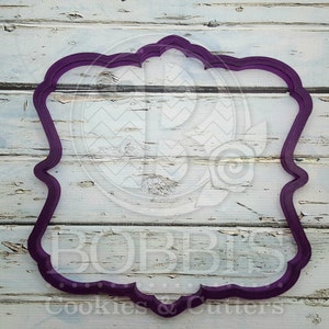 Pode incluir: Cortador de biscoitos de plástico roxo em forma de moldura decorativa com borda festonada.