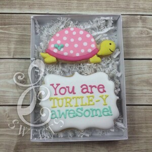May include: A white box with a pink and white polka dot turtle cookie and a white cookie with the text "You are turtle-y awesome!" in pink, yellow, and blue icing.