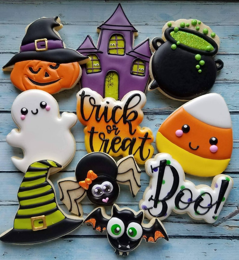 May include: A set of ten Halloween-themed sugar cookies decorated with colorful icing. The cookies feature a ghost, a spider, a bat, a witch's hat, a pumpkin, a candy corn, a cauldron, a haunted house, and the words "trick or treat" and "boo!"