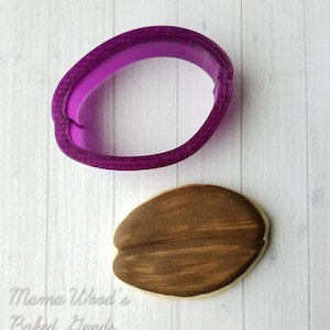 Peut inclure: Un emporte-pièce en plastique violet en forme de grain de café, à côté d'un grain de café en fondant brun et blanc.