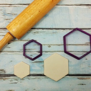 May include: A wooden rolling pin, three hexagonal cookie cutters, and three hexagonal pieces of dough on a light blue wooden surface.