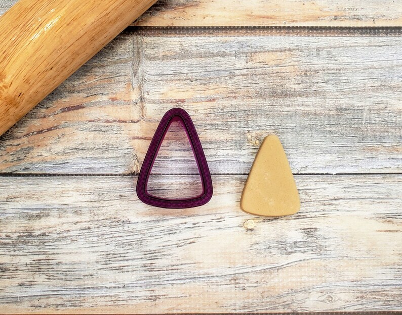 May include: A purple triangle-shaped cookie cutter and a triangle-shaped cookie on a wooden surface.