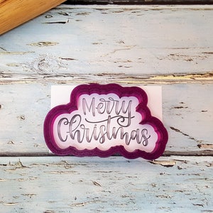 May include: A pink plastic cookie cutter shaped like a cloud with the words "Merry Christmas" written in a cursive font.