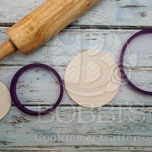 May include: A set of three purple cookie cutters in different sizes, a wooden rolling pin, and two blank round ceramic tiles.