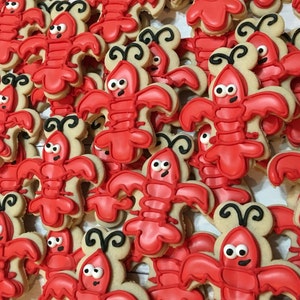 K&ouml;nnte beinhalten: Nahaufnahme eines Stapels roter und brauner Zuckerkekse, die mit Zuckerguss verziert sind, um wie Hummer auszusehen. Die Kekse sind alle unterschiedlich gro&szlig; und geformt, und einige haben schwarze Augen und F&uuml;hler.