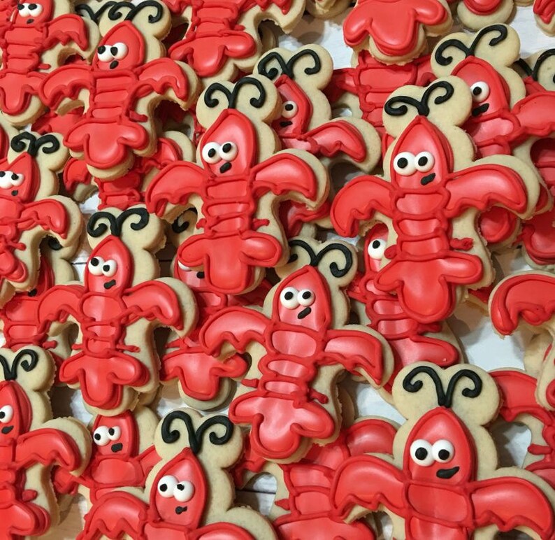 K&ouml;nnte beinhalten: Nahaufnahme eines Stapels roter und brauner Zuckerkekse, die mit Zuckerguss verziert sind, um wie Hummer auszusehen. Die Kekse sind alle unterschiedlich gro&szlig; und geformt, und einige haben schwarze Augen und F&uuml;hler.
